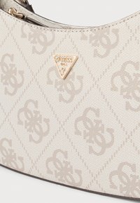 Beżowa torba wykonana z fakturowanego materiału, z wzorem diamentu i złotym trójkątnym logo. Górne zamknięcie na suwak.