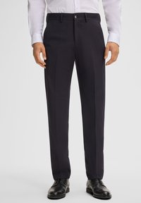 Donkerblauwe pantalon met een tailormade pasvorm, voorzien van een platte voorkant, riemlussen en een soepele stoftextuur. Gecombineerd met zwarte schoenen.