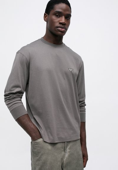 Hall sinise pikkade varrukatega särk, millel on ümardatud kaelus ja väike tikand rinnal. Valmistatud pehmest kangast ja mugavast lõikega.