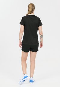 Svart tränings-t-shirt med korta ärmar, i kombination med matchande shorts. Tillverkad av lätt, andningsbar tyg. Vita accenter vid kragen.