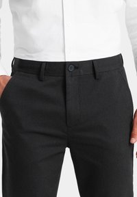 Pantalons de costume gris foncé en tissu texturé, avec une coupe standard, des passants de ceinture et une fermeture à bouton unique au niveau de la taille.