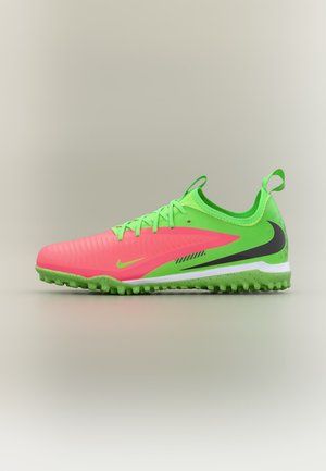 Zapatilla de fútbol de césped Nike en verde brillante y rosa con logo Swoosh negro y suela texturizada sobre un fondo neutro.