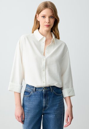 Witte button-up shirt met een textuurafwerking, opgerolde mouwen en een kraag, gecombineerd met hooggegorte blauwe denim jeans.