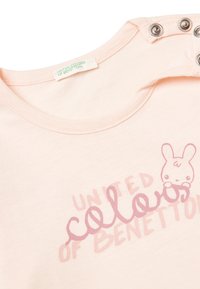 Světle růžové bavlněné tričko s kulatým výstřihem, cvočky na rameni a ilustrací kresleného králíka s textem v různých typech písma.