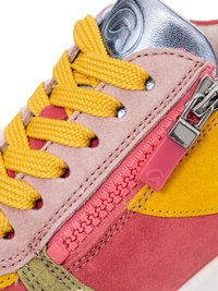 Nahaufnahme eines bunten Sneakers mit gelben Schnürsenkeln, rosa Wildleder, einem pinken Reißverschluss mit Zipper und metallisch silberner Zungenverzierung.