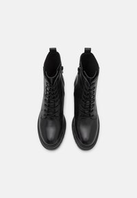 Botines de cuero negro con una superficie lisa, que cuentan con un cierre de cordones en la parte frontal, cremalleras laterales y un diseño de punta redondeada.