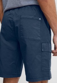 Námořnicky modré cargo kraťasy z měkké bavlny s elastickým pasem, vybavené dvěma zadními kapsami a boční cargo kapsou pro uložení věcí.