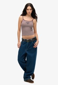 Gestreiftes Cropped Top in Kastanienrot und Weiß, kombiniert mit locker sitzenden blauen Jeans. Auffällige Details sind ein schwarzer Gürtel mit silbernen Nieten und braunen Schuhen.
