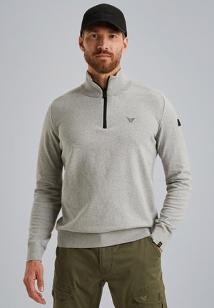 Pull en gris avec col zippé et poignets côtelés, comportant un petit logo noir sur la poitrine et un accent sur la manche gauche.