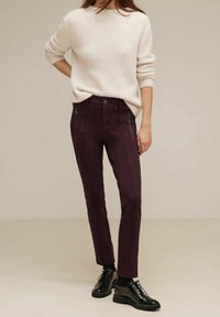 Burgundin väritetyt housut, joissa on etutaskut vetoketjulla, hienovaraiset ompeludetalit ja sileä kangas, yhdistettynä kevyeseen neulepaitaan.