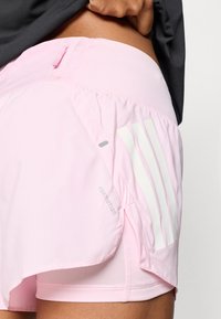 Lichtroze sportshorts met een mesh binnenvoering, voorzien van witte verticale strepen, een klein zakje en 'FORMOTION'-branding aan de zijkant.