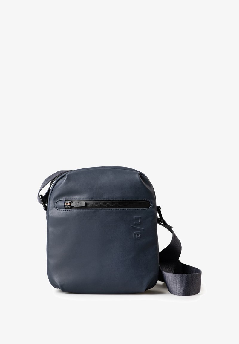 Navy crossbody bag in smooth material with a zippered front pocket, adjustable strap, and embossed logo detail on the side. Compact design.