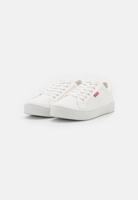 Witte canvas sneakers met een gestructureerd oppervlak, ronde neus, vetersluiting aan de voorkant en een laagprofielrubberen zool. Voorzien van een klein rood label met logo.