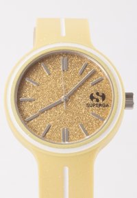 Gelbes Silikonarmband mit einem funkelnden goldenen Glitzer-Zifferblatt, silbernen Stundenmarkierungen und einem weißen Akzent um das Ziffernblatt. Silberne Krone an der Seite.