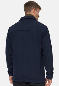 Marinblå struktureret jakke med standard krave og knapmanchetter, der har et enkelt design uden synlige logoer eller mønstre.