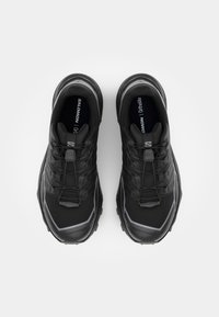 Zwarte sportschoenen met een gestructureerde bovenkant, reflecterende accenten en een gestepte zool. Voorzien van elastische veters en een logo aan de zijkant.