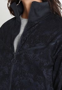 Námořnická bunda na zip s texturovaným vzorem, vysokým límcem a vyšívanými detaily. Doplňena postranními kapsami a hladkým materiálem.