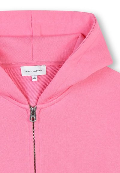Felpa rosa con zip e colletto alto, caratterizzata da una cerniera argentata e un'etichetta cucita che riporta la scritta "MARC JACOBS". Texture liscia.