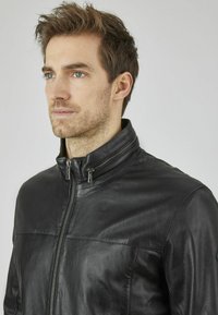 Chaqueta de cuero negro con cuello alto y cierre frontal de cremallera. Presenta una textura suave y un diseño limpio con costuras mínimas.