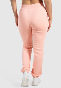 Sweatpants i blød ferskenfarvet stof, med elastisk talje og ribbede manchetter, der fremhæver en afslappet pasform og glat tekstur.