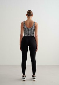 Juodai-balta houndstooth rašto maikutė su žemu atlenkimu, derinama su juodomis aukšto juosmens tamprėmis ir білomis sportinėmis bateliais. Lygus paviršius.