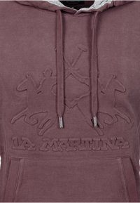 Brun hoodie med en texturerad logotyp med ridsportmotiv, justerbara dragsko och en framficka i kängurustil. Tillverkad av mjukt tyg.