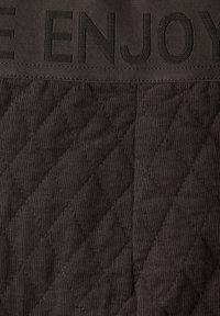 Tummanharmaa tikattu kangas, jossa on vinoneliönmuotoisia kuvioita; yläosassa kohokuvioitua tekstiä. Pehmeä rakenne, kestävä materiaali.