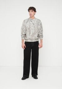 Γκρι φούτερ με διακριτικό μοτίβο δάσους, συνδυασμένο με μαύρο παντελόνι φαρδύ και μαύρα παπούτσια. Το ύφασμα φαίνεται μαλακό με άνετη εφαρμογή.