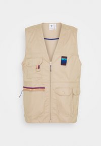 Beige zip-väst med flera fickor, en färgglad mönstrad detalj runt dragkedjan och en broderad logotyp patch på bröstområdet.