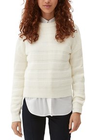 Gehaakte trui in crème met horizontale textuurstrepen, ronde halslijn en ribgebreide manchetten. Gedragen over een witte blouse met kraag.