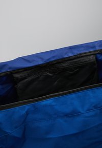 Bolsa de tela azul con una cremallera en la parte superior, que cuenta con un bolsillo interior negro y un material de textura suave. Interior espacioso con un diseño sencillo.