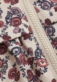 Blommigt mönstrad tyg i nyanser av burgundy, rosa och marinblått på en beige bakgrund, med en framträdande cremefärgad dragkedja.