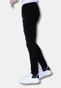 Zwarte slim-fit denim jeans met versleten details op de knieën, gecombineerd met witte sneakers met zwarte accenten.