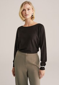 Fekete, hosszú ujjú kötött felső, magas derekú bézs nadrággal párosítva. Finom fénylés, laza szabás, egyszerű textúra és minimalista dizájn.