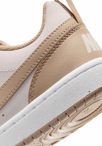 Κοντινό πλάνο της φτέρνας αθλητικού παπουτσιού σε μπεζ και λευκό χρώμα με υφή στη σόλα και εμφανείς ραφές.