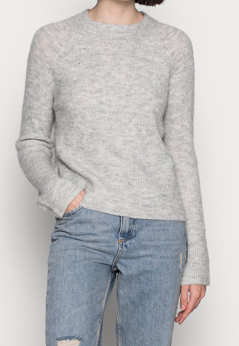 Grijze gebreide trui met een ronde hals, geribbelde textuur en lange mouwen. Casual pasvorm, gecombineerd met versleten lichtblauwe jeans.