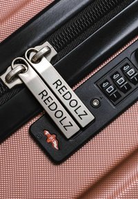 Primer plano de una maleta texturizada rosa con cremallera negra y candado de combinación establecido en 000, con tiradores de cremallera etiquetados como REDOLZ.
