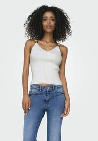 Geribbelde witte tanktop met een V-hals en gouden accenten op de bandjes, gecombineerd met mid-rise blauwe spijkerbroek.