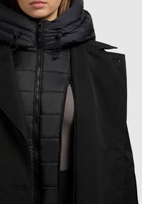 Czarna wielofunkcyjna odzież wierzchnia z puchową, ocieploną warstwą wewnętrzną, wysokim kołnierzem i gładkim wykończeniem z detalami zamka błyskawicznego.