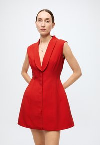 Red sleeveless dress with a deep V-neckline, structured bodice, and flared skirt. Smooth fabric with clean lines and no visible patterns.