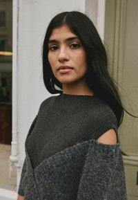 Dunkelgrauer, gerippter Strickpullover mit ausgeschnittenen Schultern und strukturierten Akzenten. Der Stoff wirkt weich mit einem lockeren, mehrlagigen Design.