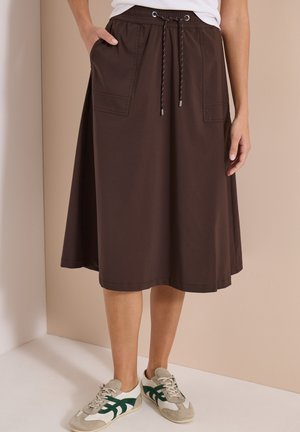 Jupe marron longueur genou avec poches avant et taille à cordon, portée avec des baskets blanches et vertes.