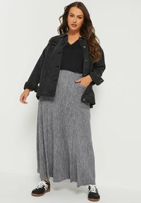Veste en denim noir sur un top noir à col en V, associée à une jupe maxi plissée grise. Présente des baskets avec des accents noir et blanc.