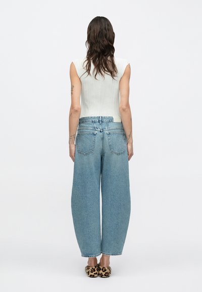 Εφαρμοστή ανοιχτό γκρι φανέλα, τζιν παντελόνι μπλε με ψηλή μέση και φαρδιά μπατζάκια, ακατέργαστο τελείωμα, πίσω τσέπες, παπούτσια με λεοπάρ σχέδιο. Το μοντέλο φαίνεται από πίσω.