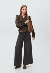 Blusa con stampa leopardata marrone e maniche a sbuffo, abbinata a jeans neri a gamba larga e stivali alla caviglia marroni. Borsa marrone come accessorio di rilievo.