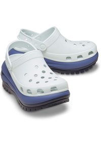 Zuecos de plástico blancos con orificios de ventilación, con una suela exterior de color azul marino en contraste y una correa trasera para un ajuste seguro.