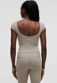 Aansluitende top met korte mouwen van zacht beige materiaal, met een brede ronde opening op de rug. Gekleed met bijpassende beige leggings, die een naadloos ontwerp laten zien.
