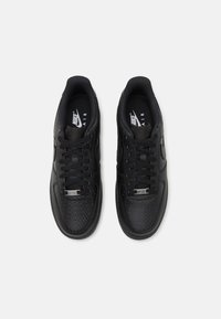 Black athletic sneakers featuring a textured finish, round laces, and a silver logo accent on the tongue. Smooth and sturdy material.