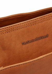 Interno di una borsa in pelle marrone con cuciture visibili e lettering impresso che recita "The Chesterfield Brand." Texture liscia, design pulito.