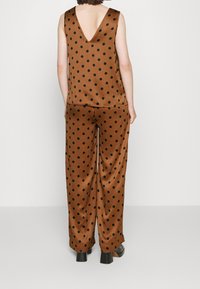 Tenue en satin brun avec des pois noirs, comprenant un haut sans manches et un pantalon à jambes larges. Le haut présente un profond décolleté en V dans le dos.